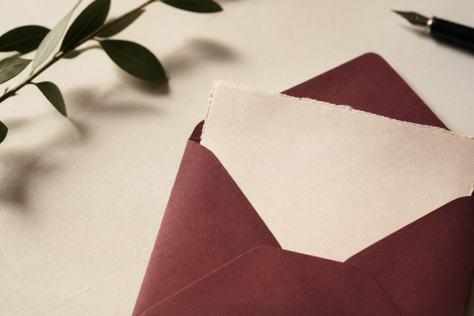 A cream card in a burgundy envelope beside greenery